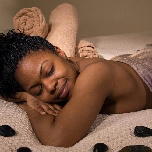 Woman enjoying relaxation during a spa treatment with soothing stones and towels, promoting self-care with the Imphepho body care gift set.
