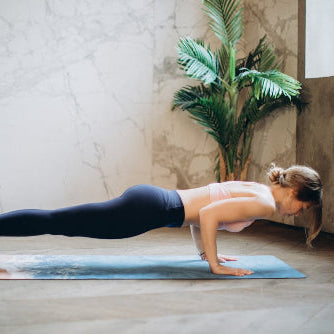 Woman performing a yoga pose on a mat in a room with a plant and neutral decor.