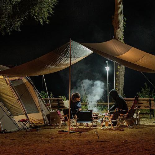 campers relaxing by a fire under a tent at night, enjoying outdoor camping atmosphere whilst using lavender tea tree roll-on
