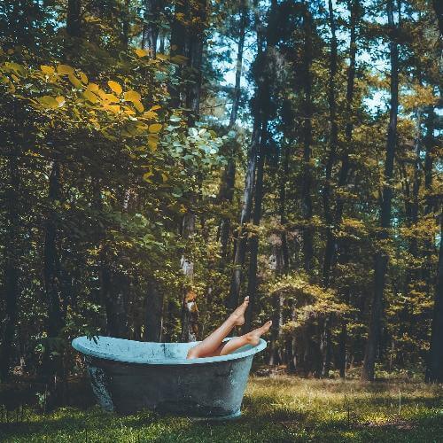 Relaxing in a rustic bathtub surrounded by trees, promoting serenity and self-care with cold flu immunity soak bath salts.