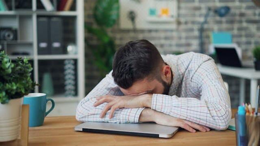 A man resting his head on a laptop, embodying signs you need better sleep in a home office setting.