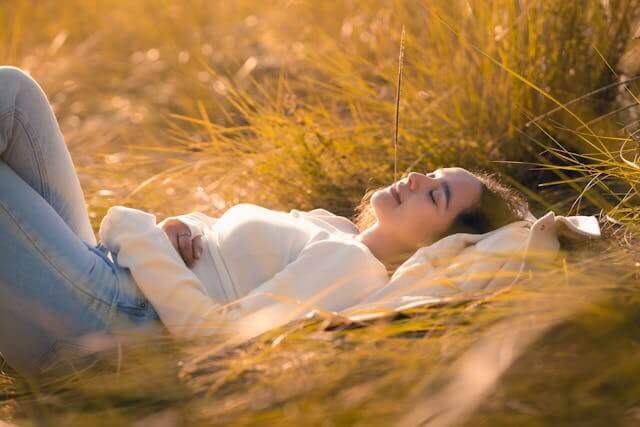 A woman practicing natural sleep rituals South Africa, relaxing on grass in a serene outdoor setting.