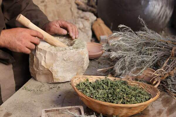 hands grinding herbs in a mortar with natural herbal supplements story components and a basket of dried leaves
