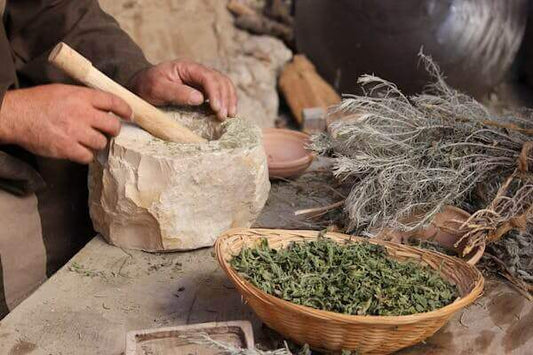 hands grinding herbs in a mortar with natural herbal supplements story components and a basket of dried leaves