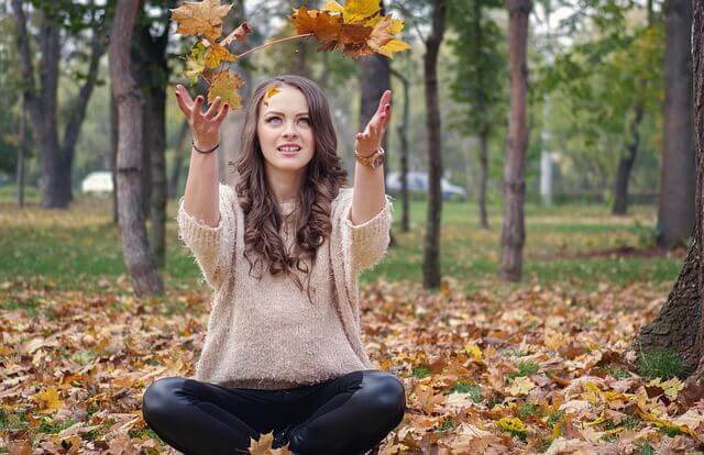 Woman enjoying autumn wellness rituals South Africa while playing with falling leaves in a serene park.