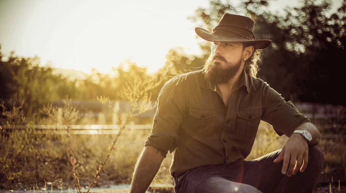 Man wearing a hat with a beard enjoying nature during sunset for Movember self-care essentials.