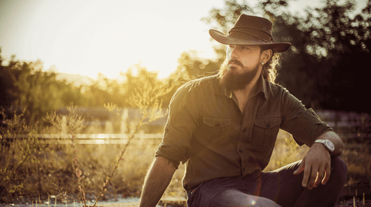Man wearing a hat with a beard enjoying nature during sunset for Movember self-care essentials.