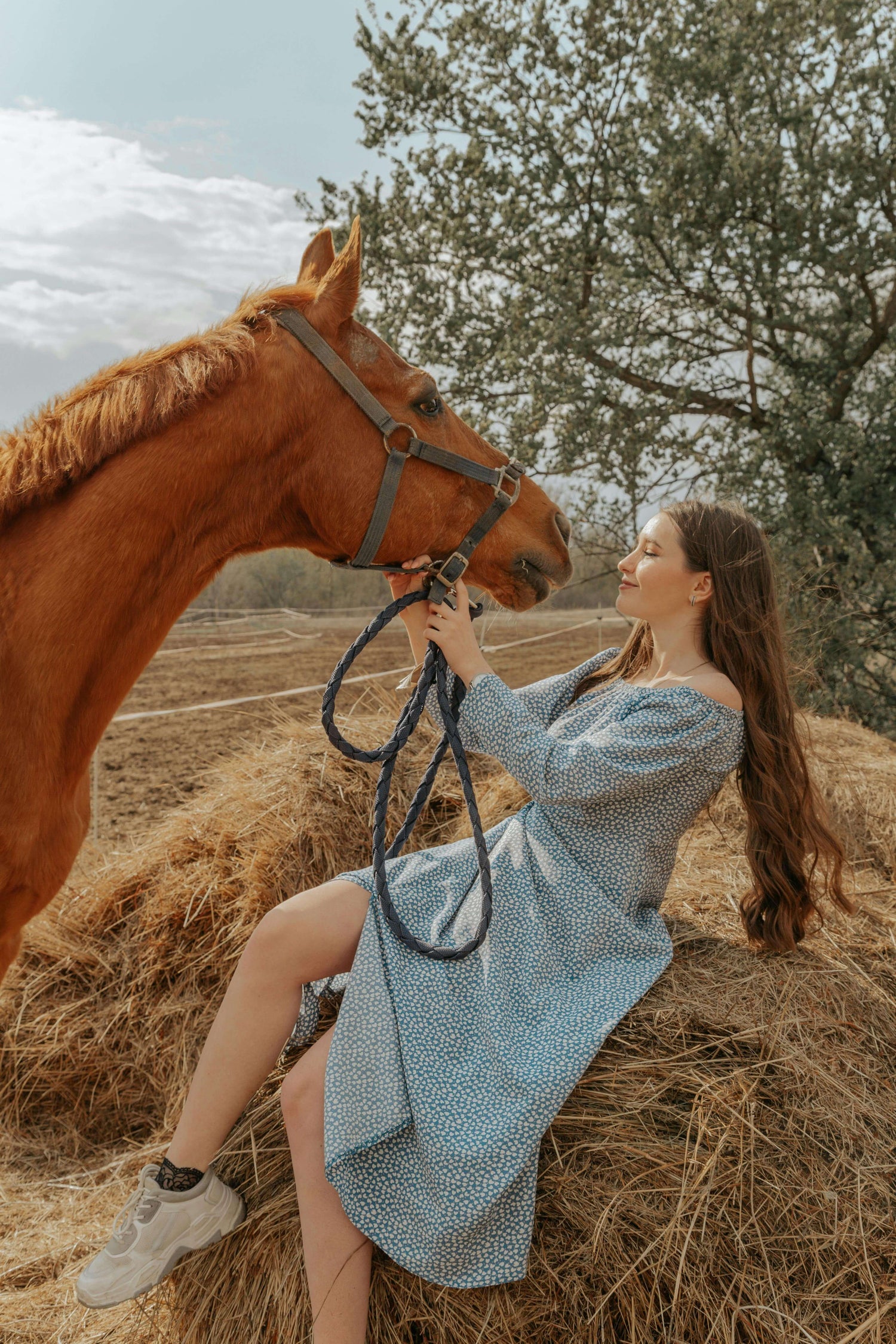 Woman in a blue dress interacts lovingly with a horse in a serene farm setting ,symbolising women's wellness collection 