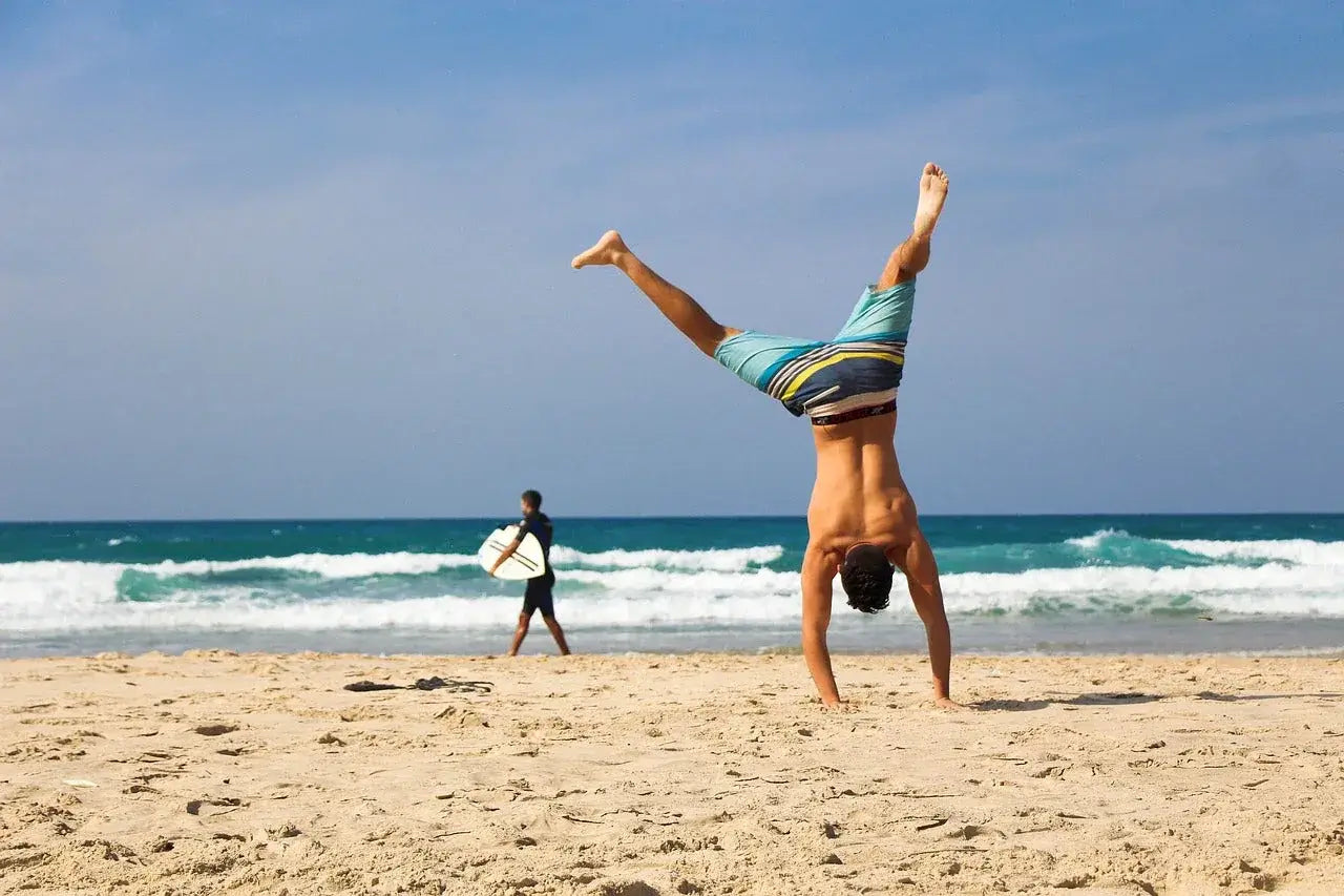 Young man doing a handstand on the beach, embodying youthful lifestyle tips and vitality in a sunny setting.